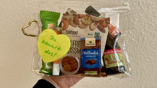 Foto Prüfungs-Survival-Kit von vorn: ein durchsichtes Täschcen mit verschiedenen Dingen (Vitaminshot, Mini-Tafel Schokolade, Herz mit der Aufschrift "Du kannst das!" u.a.